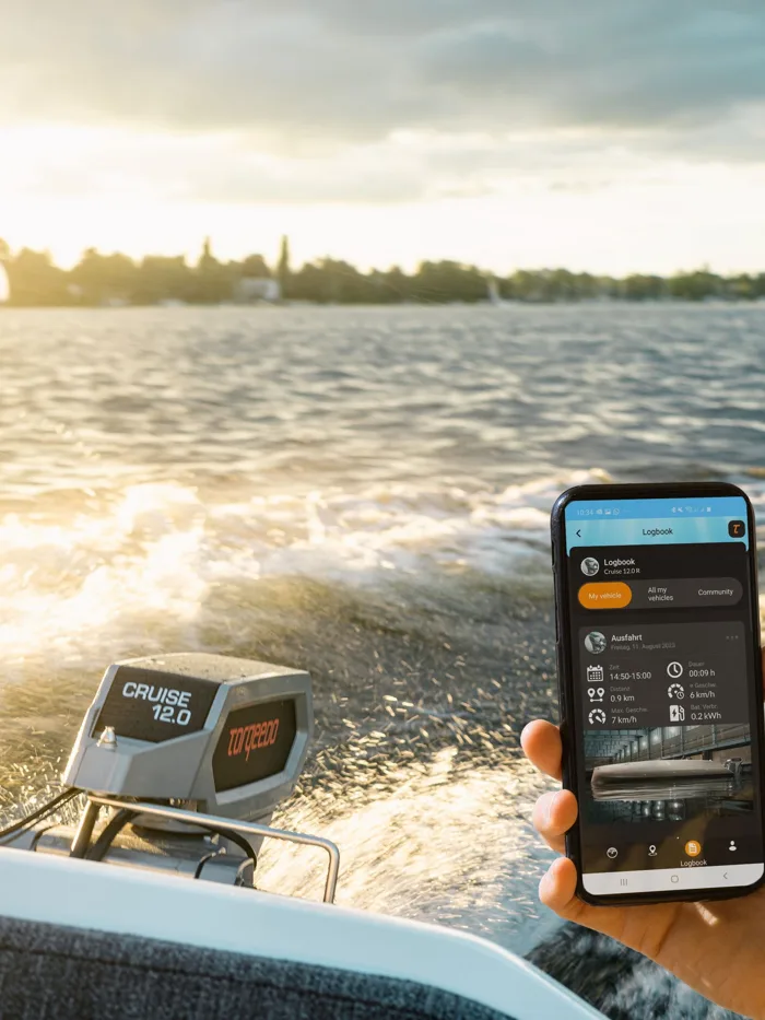 A Torqeedo Cruise electric outboard at speed, with the owner holding the phone app open on the trip logbook